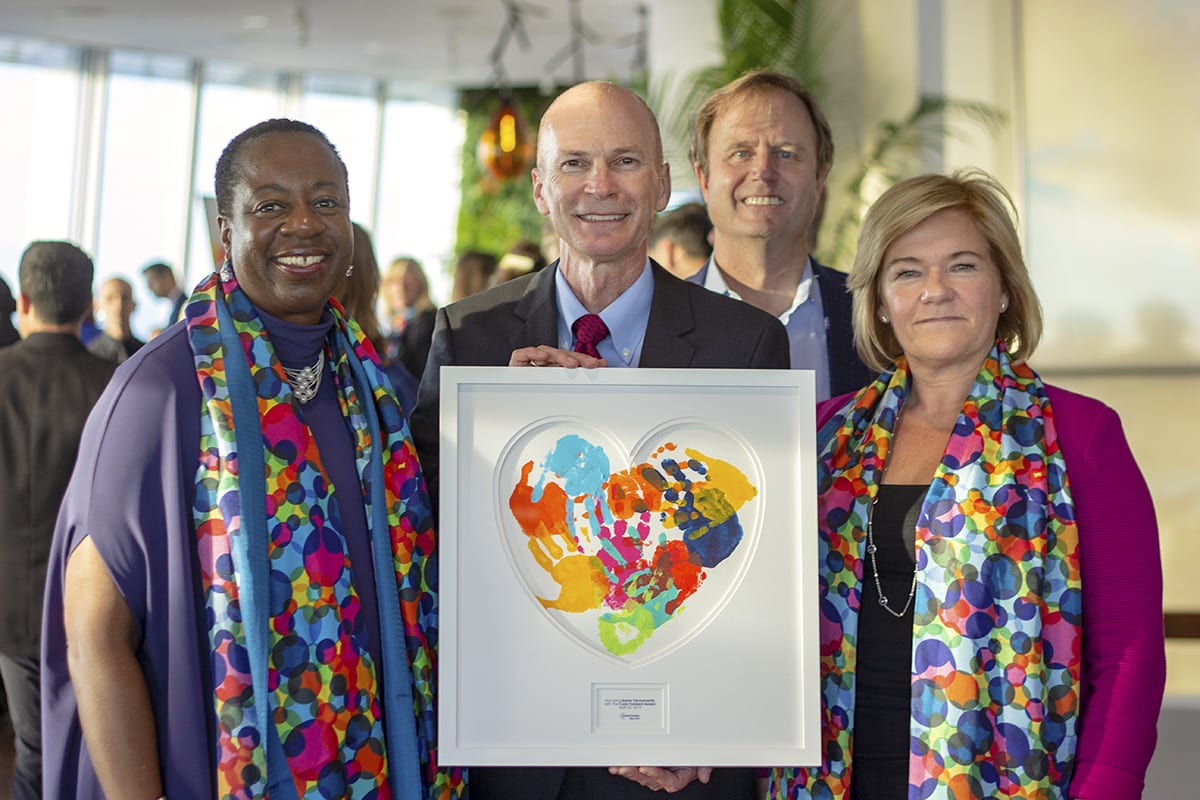 four people smiling and holding a painting of children's handprints