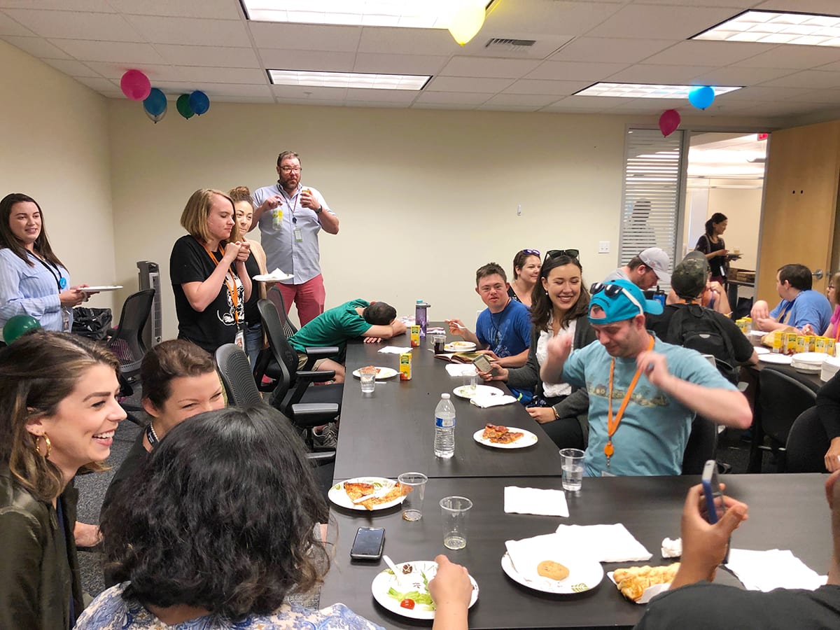 group of people sitting at tables eating pizza and laughing